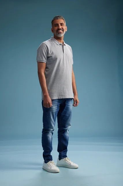 رجل سعودي بملابس كاجوال يقف في استوديو بخلفية زرقاء