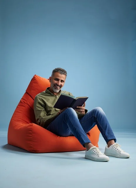 رجل سعودي يقرأ كتابا على كنبة كيس برتقالية في استوديو