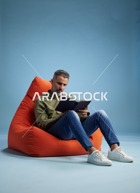 رجل سعودي يقرأ كتاباً على كنبة كيس برتقالية