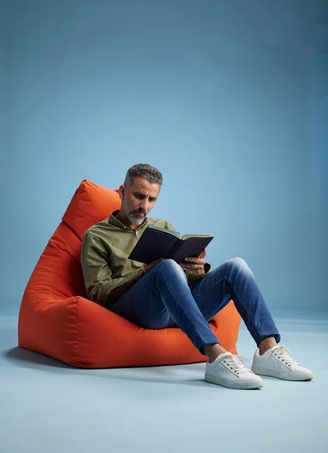 رجل سعودي يقرأ كتاباً على كنبة كيس برتقالية
