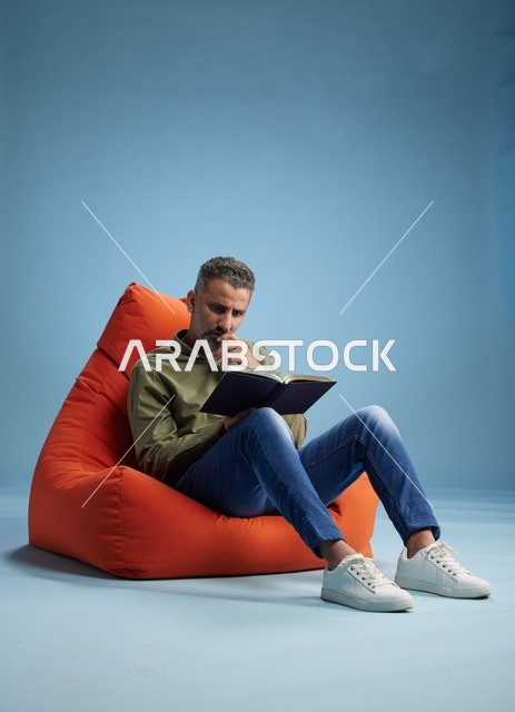 رجل سعودي يقرأ كتاباً على كنبة كيس برتقالية