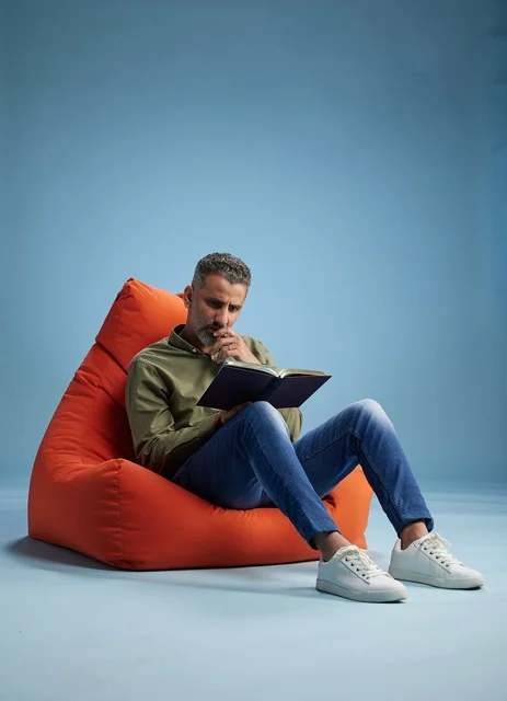 رجل سعودي يقرأ كتاباً على كنبة كيس برتقالية