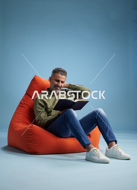 رجل سعودي يقرأ كتاباً على كنبة كيس برتقالية في الاستوديو