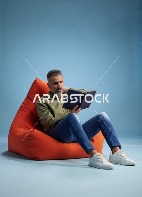 رجل سعودي يقرأ كتاباً على كنبة كيس برتقالية