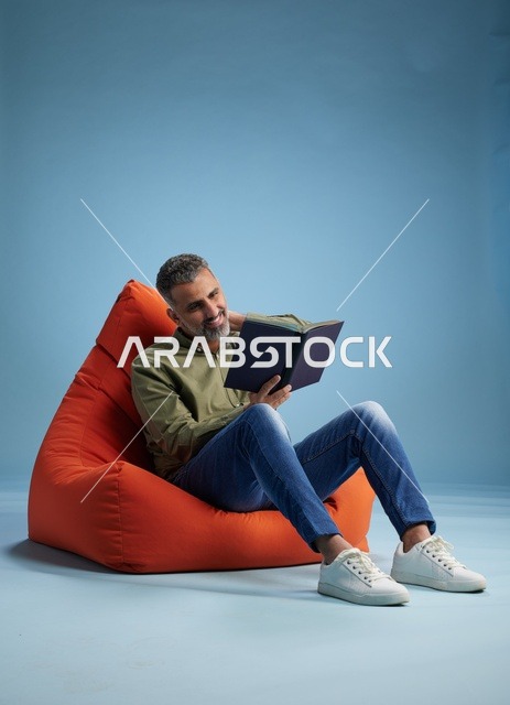 رجل سعودي يقرأ كتاباً على كنبة كيس حمراء