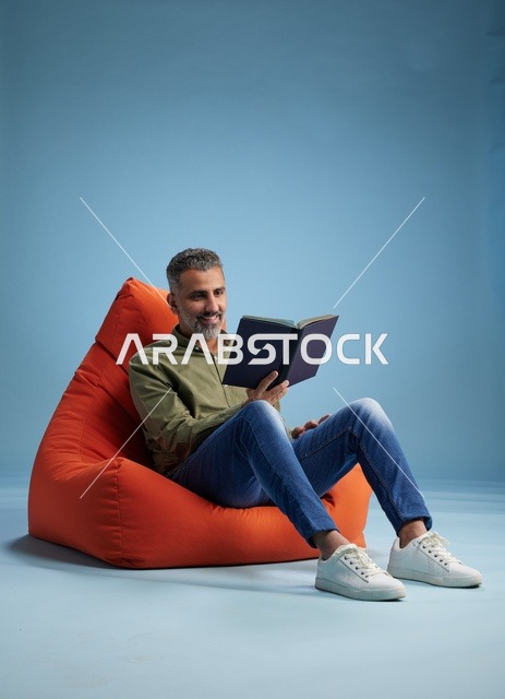 رجل سعودي يقرأ كتاباً على كنبة كيس برتقالية