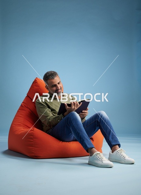 رجل سعودي يقرأ كتاباً على كرسي بين باج برتقالي