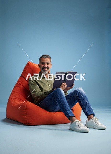 رجل سعودي يقرأ كتاباً على كنبة كيس برتقالية