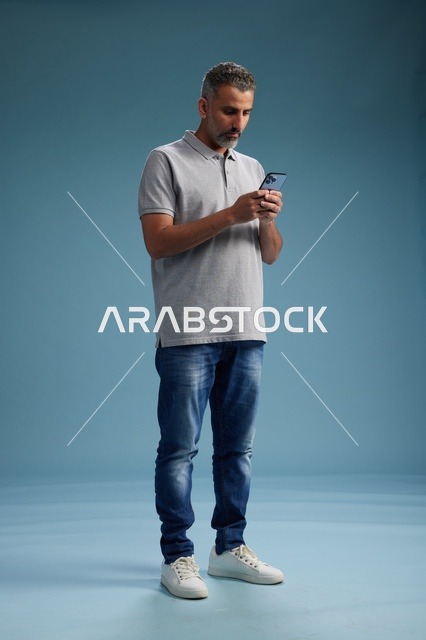 Saudi Man Using Smartphone on Blue Studio Background
