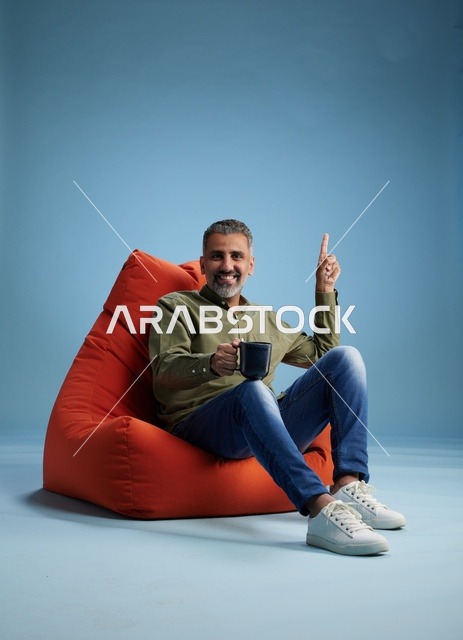 Saudi Man on Beanbag Chair Pointing Up with Coffee Mug