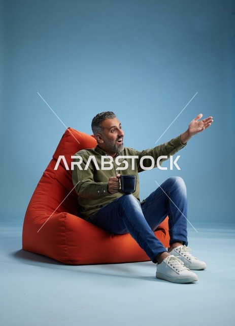 رجل سعودي على كنبة كيس حمراء مع فنجان قهوة