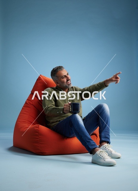 رجل سعودي على كنبة كيس برتقالية مع فنجان قهوة