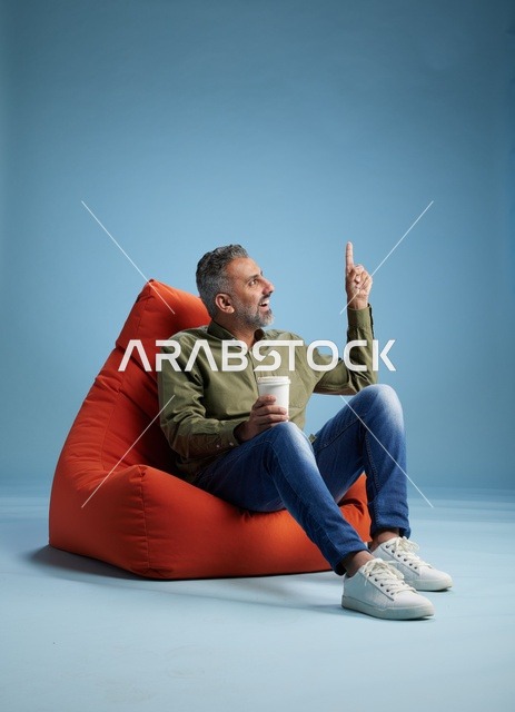 رجل سعودي جالس على كنبة كيس يشير للأعلى