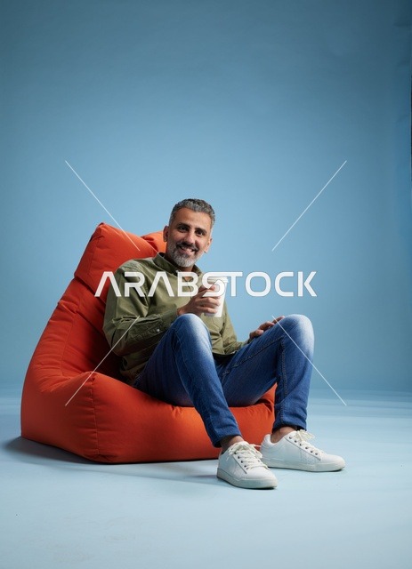 رجل سعودي يجلس على كنبة كيس برتقالية مع قهوة