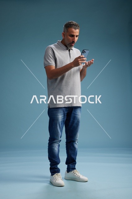 Surprised Saudi Man Using Smartphone on Blue Background