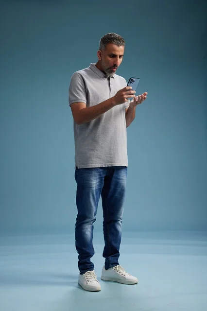 رجل سعودي متفاجئ يستخدم الهاتف الذكي بخلفية زرقاء