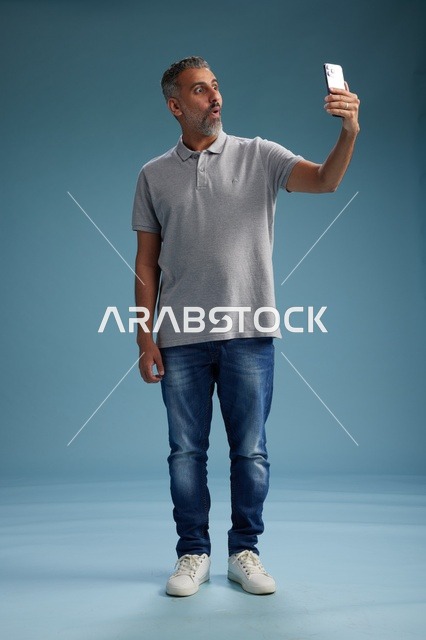 رجل عربي متفاجئ يحمل هاتفاً ذكياً بخلفية زرقاء