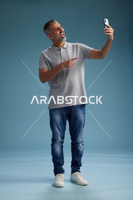 رجل عربي في منتصف العمر يشير لهاتفه في استوديو