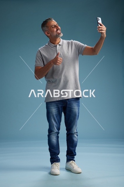 Arab Man Taking Selfie with Thumbs Up on Blue Background