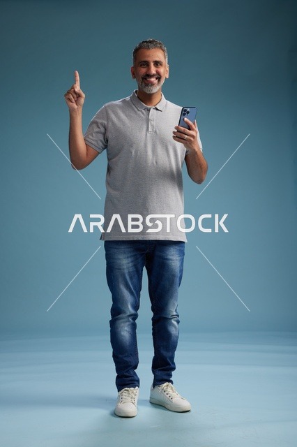رجل سعودي يحمل هاتف ذكي ويشير للأعلى في استوديو