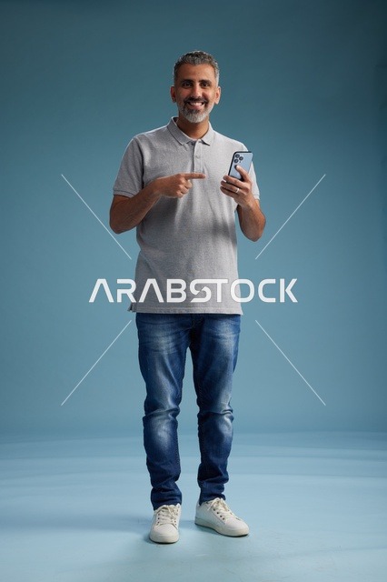 رجل سعودي مبتسم يشير إلى هاتف ذكي في الاستوديو