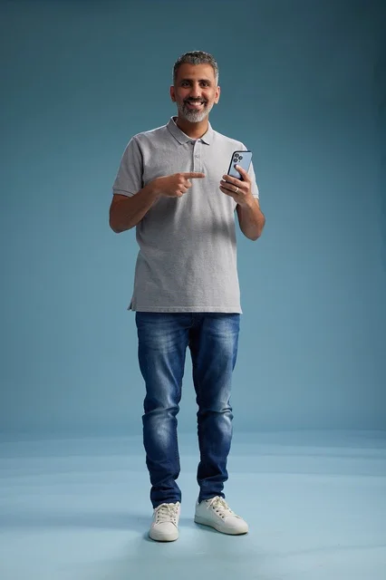 رجل سعودي مبتسم يشير إلى هاتف ذكي في الاستوديو