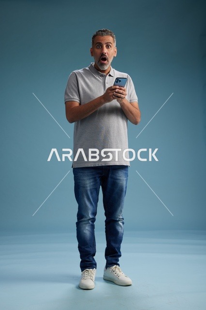 رجل عربي مندهش مع هاتف ذكي على خلفية استوديو زرقاء
