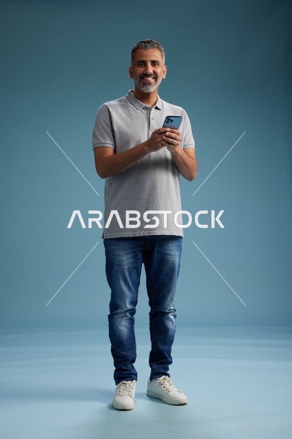 رجل سعودي في منتصف العمر يحمل هاتف ذكي في استوديو أزرق