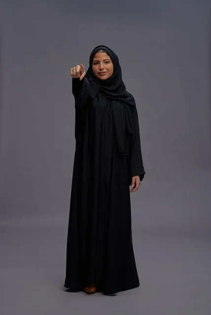 امرأة سعودية بالعباءة السوداء تشير إلى الكاميرا