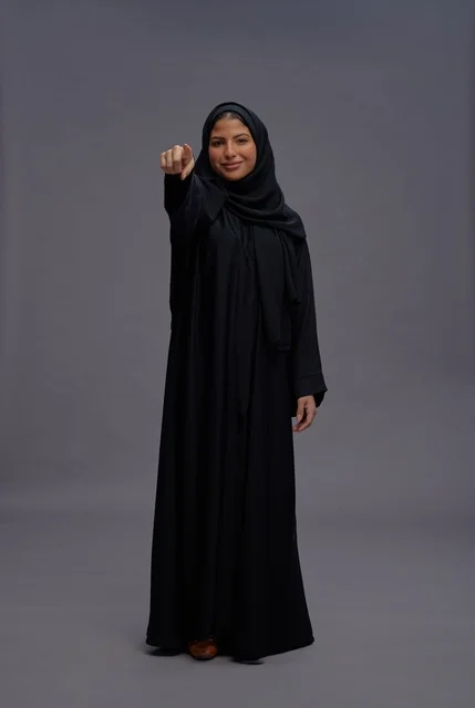 امرأة سعودية بعباءة سوداء تشير نحو الكاميرا