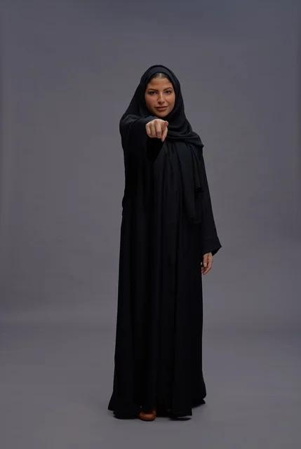 امرأة سعودية بالعباءة السوداء تشير نحو الكاميرا