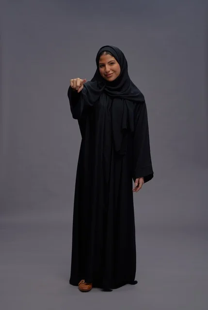امرأة سعودية بالعباءة السوداء تشير نحو الكاميرا