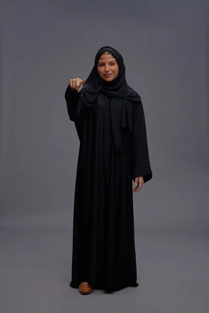 امرأة سعودية بالعباءة السوداء تشير نحو الكاميرا