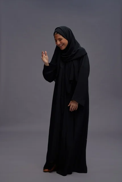 امرأة سعودية بالعباءة السوداء تضحك في الاستوديو