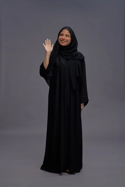 امرأة سعودية بالعباءة السوداء تلوح أمام خلفية رمادية