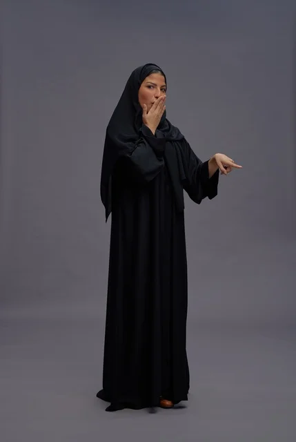 امرأة سعودية بالعباءة تشير بتعبير وجه متفاجئ
