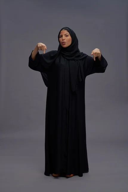 امرأة سعودية بعباءة سوداء تشير للأسفل في الاستوديو