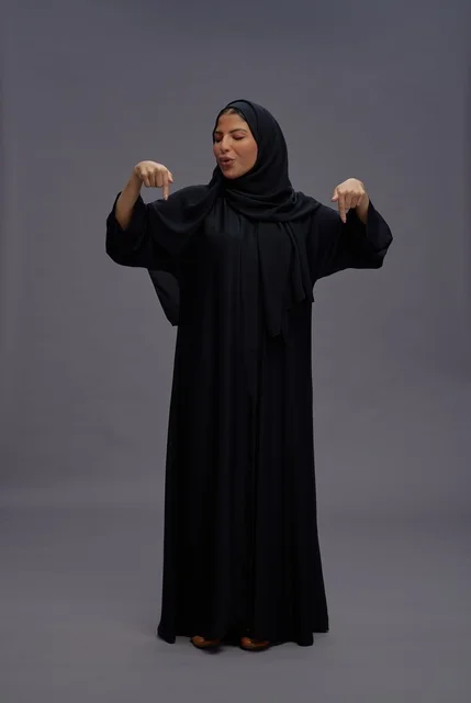 امرأة سعودية بالعباءة السوداء تشير للأسفل في استوديو