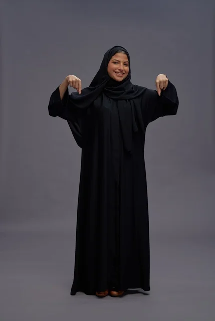 امرأة سعودية بالعباءة السوداء تشير للأسفل في الاستوديو
