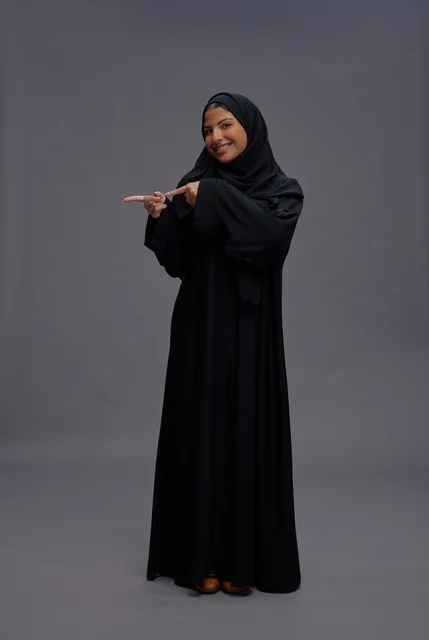 امرأة سعودية بعباءة سوداء تشير للجانب في الاستوديو