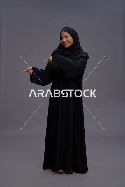 Saudi Woman in Abaya Pointing on Grey Background