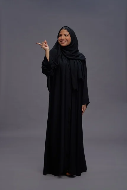 امرأة سعودية بالعباءة السوداء التقليدية تشير للجانب