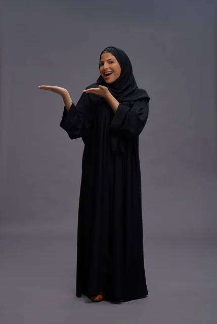 امرأة سعودية بالعباءة السوداء تشير في استوديو رمادي
