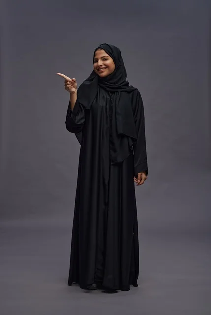 امرأة سعودية بالعباءة تشير على خلفية رمادية