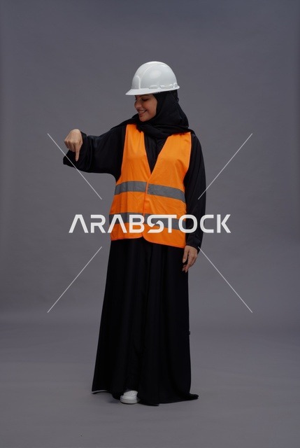 مهندسة عربية ترتدي سترة السلامة وتشير للأسفل في استوديو