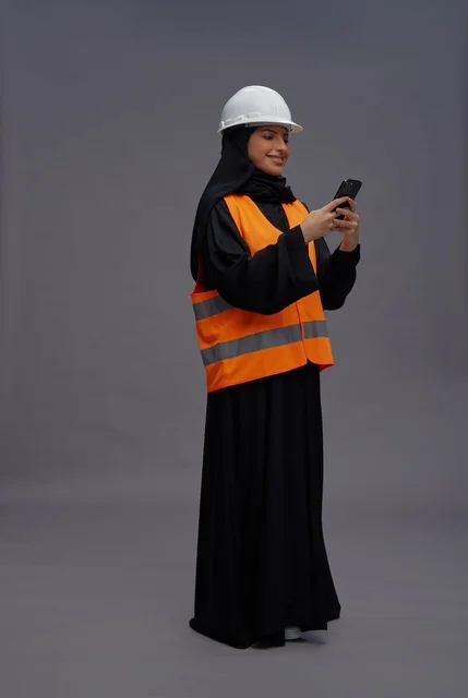 Saudi Female Engineer in Safety Vest Using Smartphone