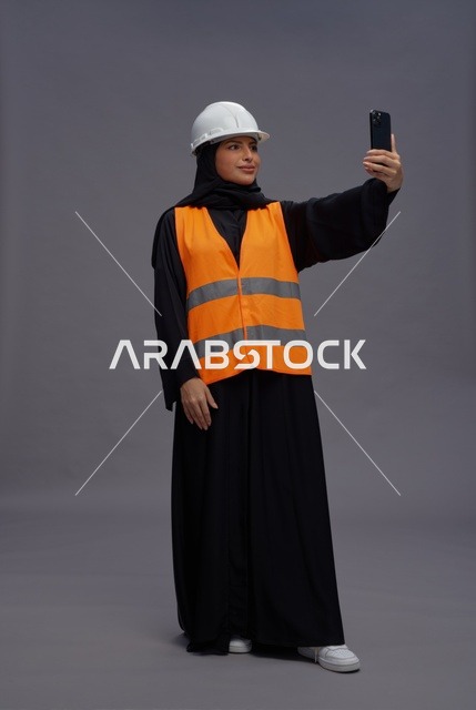 مهندسة عربية ترتدي سترة السلامة وتستخدم الهاتف