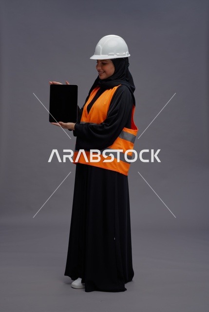 مهندسة سعودية تحمل جهاز لوحي بخوذة سلامة بيضاء