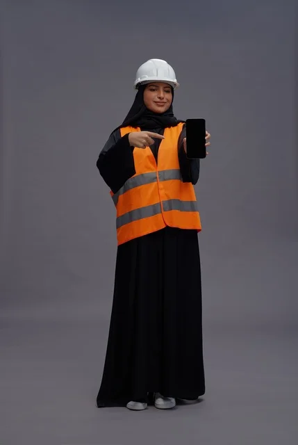 مهندسة سعودية تمسك هاتف ذكي بملابس السلامة في الاستوديو