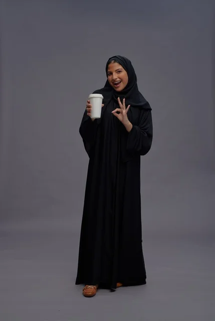 امرأة سعودية بالعباءة السوداء تحمل كوب قهوة